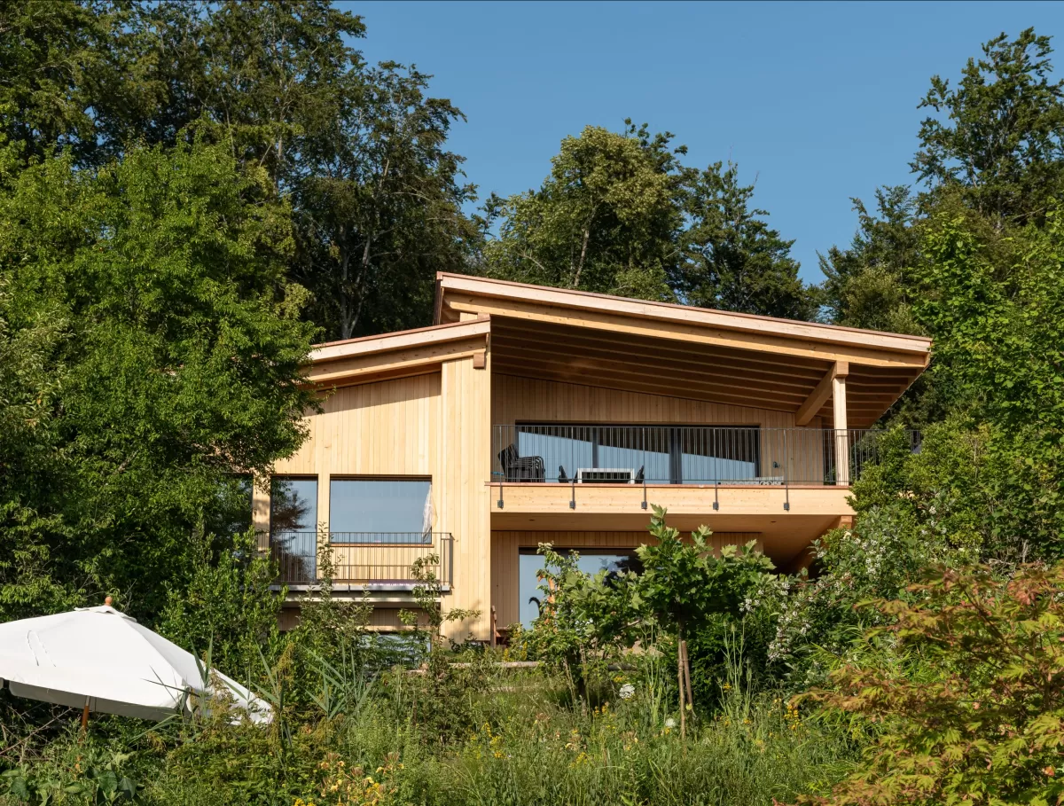 Truberholz Einfamilienhaus mit integrierter Arven-Täfer Wand. Schlafzimmer mit integrierter Dusche und Waschtisch. In der Dusche ist eine Brettstappel-Decke und der Boden ist aus ein Eschen Riemenboden. Die Wände sind Truberholz sichtbar. Die Decke ist leicht in der Dachschräge und ist eine Massivholzplatte. In der Wohnstube ist ein Cheminée mit Sitzoffen/Sitzbank.