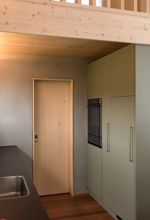 Truberholz Mehrfamilienhaus. Aussenschalung vor vergrautes Falzbrett aus Tanne, integrierte Sauna in Ferienwohnung, Saunawand aus Tanne, Möbel in der Saune aus Arven Holz, Truberholz-Wände innen sichtbar, inklusive Decke Dachschräge, Gebäudehülle Truberholz sichtbar, Innendecke Brettstapel, Boden ist alles Trockenbauaufbau, Zimmer und Bad aus Tannen Holz und allgemein Räume sind Buchenriemenboden. Türen sind alle Massivholz mit Blockfutter aus Tanne.