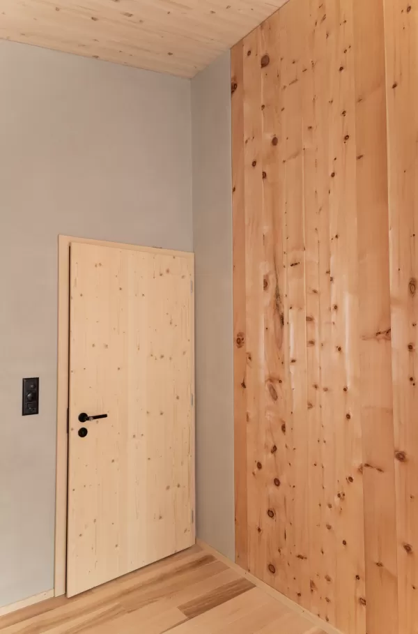 Truberholz Einfamilienhaus mit integrierter Arven-Täfer Wand. Schlafzimmer mit integrierter Dusche und Waschtisch. In der Dusche ist ein Brettstappel-Decke und der Boden ist aus ein Eschen Riemenboden. Die Wände sind Truberholz sichtbar. Die Decke ist leicht in der Dachschräge und ist eine Massivholzplatte. In der Wohnstube ist ein Cheminée mit Sitzoffen/Sitzbank.