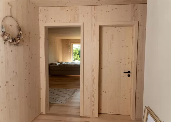 Truberholz Einfamilienhaus mit integrierter Arven-Täfer Wand. Schlafzimmer mit integrierter Dusche und Waschtisch. In der Dusche ist ein Brettstappel-Decke und der Boden ist aus ein Eschen Riemenboden. Die Wände sind Truberholz sichtbar. Die Decke ist leicht in der Dachschräge und ist eine Massivholzplatte. In der Wohnstube ist ein Cheminée mit Sitzoffen/Sitzbank.