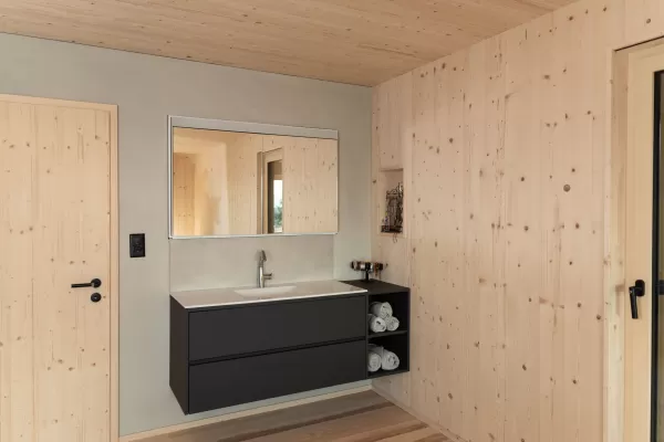 Truberholz Einfamilienhaus mit integrierter Arven-Täfer Wand. Schlafzimmer mit integrierter Dusche und Waschtisch. In der Dusche ist ein Brettstappel-Decke und der Boden ist aus ein Eschen Riemenboden. Die Wände sind Truberholz sichtbar. Die Decke ist leicht in der Dachschräge und ist eine Massivholzplatte. In der Wohnstube ist ein Cheminée mit Sitzoffen/Sitzbank.