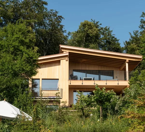 Truberholz Einfamilienhaus mit integrierter Arven-Täfer Wand. Schlafzimmer mit integrierter Dusche und Waschtisch. In der Dusche ist ein Brettstappel-Decke und der Boden ist aus ein Eschen Riemenboden. Die Wände sind Truberholz sichtbar. Die Decke ist leicht in der Dachschräge und ist eine Massivholzplatte. In der Wohnstube ist ein Cheminée mit Sitzoffen/Sitzbank. 